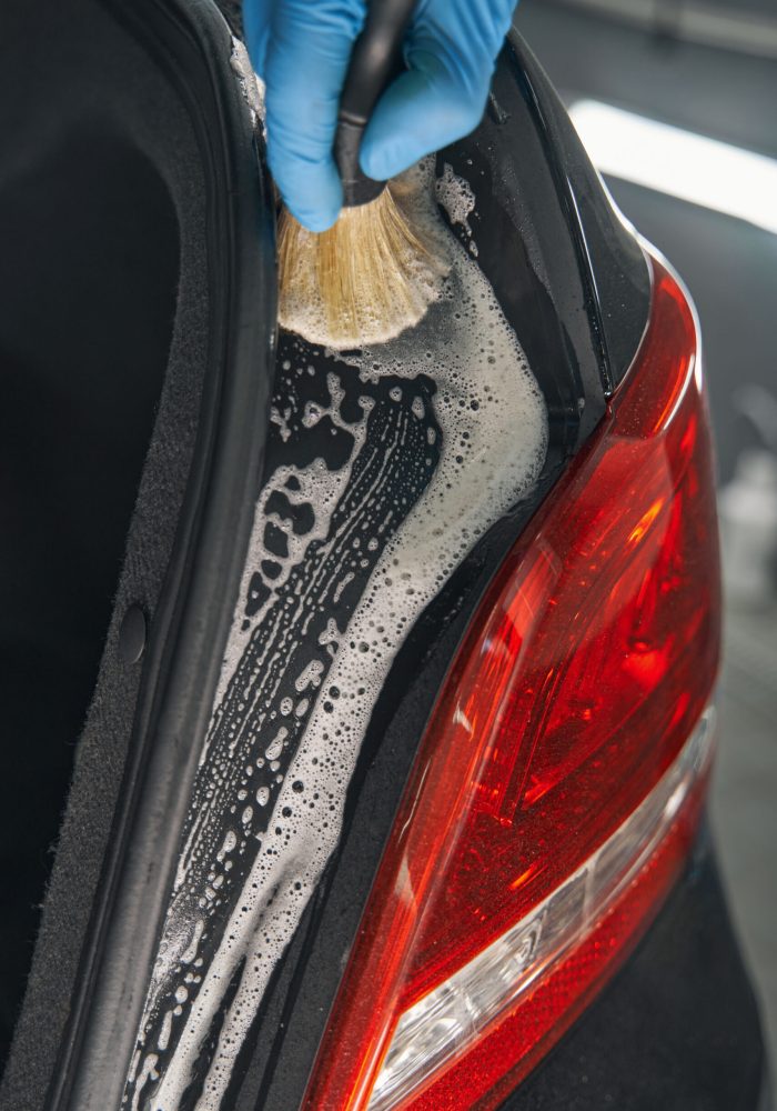 Service worker cleaning car with washing fluid and brush during detailing
