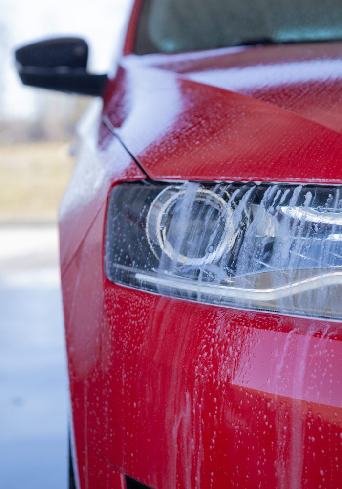 Car wash close-up. Washing a modern car with high-pressure water and soap, cleaning the headlights